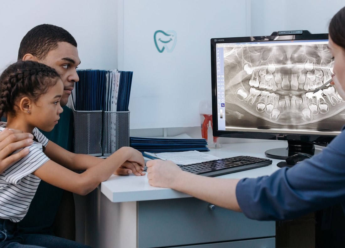 A father and his young daughter listening as a dentist explains an X-ray on a screen